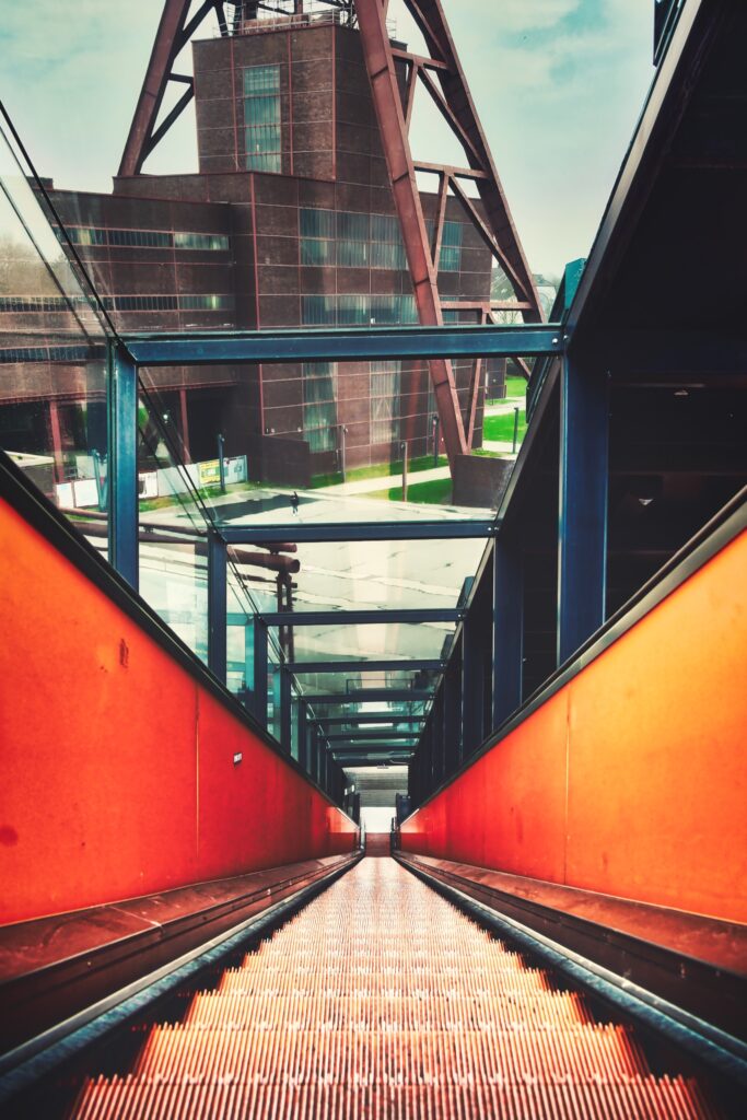 Zeche Zollverein - Orangefarbene Rolltreppe mit Gebäude des Schacht XII im Hintergrund